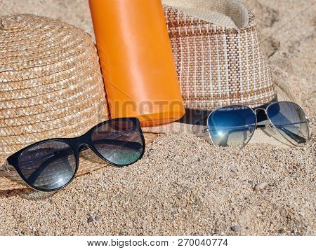 Two Sunhats, Sunglasses And Sunprotection Cream Are Laying On The Sand.
