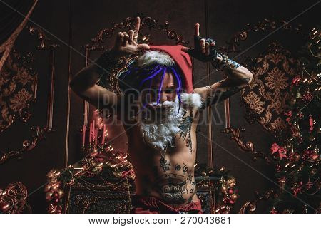 Bad Santa concept. Portrait of a nude tattooed Santa with purple dreads demonstrating antisocial behavior, rudeness and aggression. 