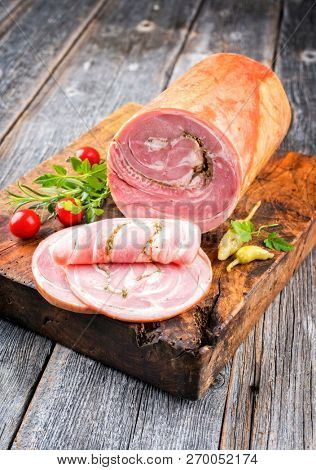 Traditional Allgauer veal roast roll sausage sliced and as piece with tomatoes and chili as closeup on an old rustic cutting board