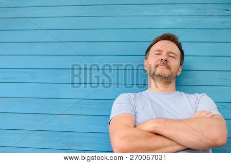 Shot Of Handsome Mature Man Crossing Hands And Look At Camera. Male Portrait With Blue Wooden Wall O