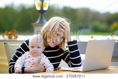 Tired Young Mother Working Oh Her Laptop And Holding 6-month Daughter