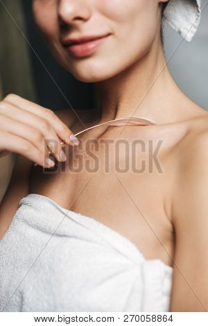 Close up pof pretty young woman wrapped in towel holding a feather indoors