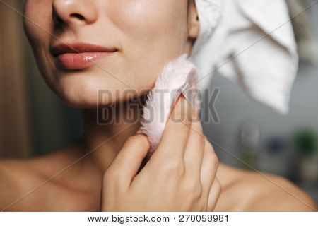 Beautiful young woman wrapped in bath towel standing at the bathroom, using powder puff