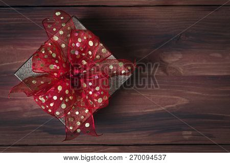 One Classic Red Gift Box Golden Bow On Natural Wood Background, Soft Blur Focus At The Left Area For