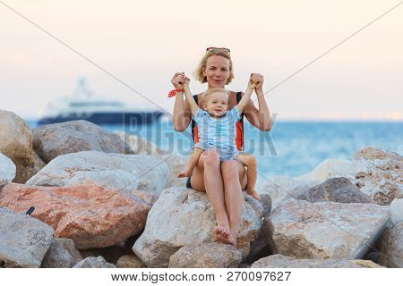 Woman Playing With Her Baby Outside Against The Sea. The Concept Of A Happy Full-fledged Family Life