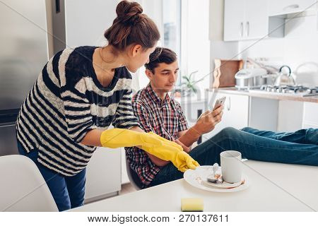 Lazy Boyfriend Hanging In Phone While His Girlfriend Cleaning His Dishes After Dinner In Kitchen. Fa