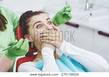 Frightened Girl At Dentist Office Covered Mouth With Hands. Concept Phobia Dental Office.