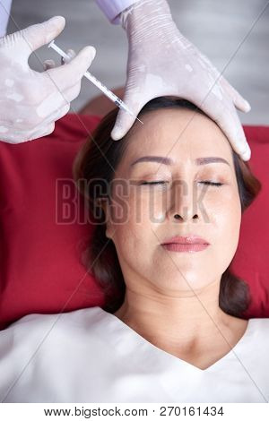 Vietnamese Middle-aged Woman Getting Forehead Botox Injection At Cosmetologist