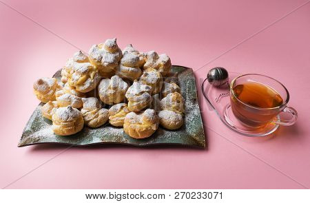 Delicious Eclairs Sprinkled With Icing Sugar And Cup Of Tea On A Pink Background. Homemade Profitero