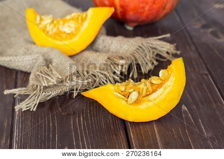 Group Of One Whole Two Slices Of Fresh Red Kuri Pumpkin Hokkaido Variety On Jute Cloth On Brown Wood