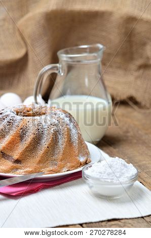 Homemade Bundt Cake Sprinkled With Sugar, Milk And Eggs In Background