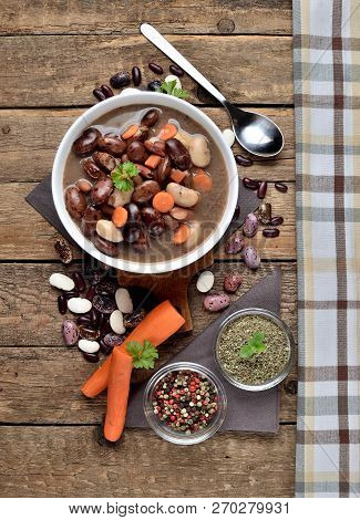 Close-up Of Full Bowl Of Hot Bean Soup With Large Beans On Cutting Board, Carrots, Parsley, Marjoram