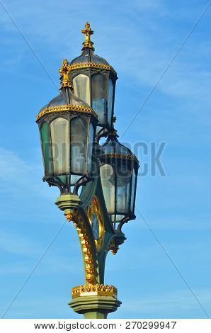 A Lamp-post With Three Glass Lanterns Is Seen Against A Blue Sky With Pale White Clouds. The Lamps H