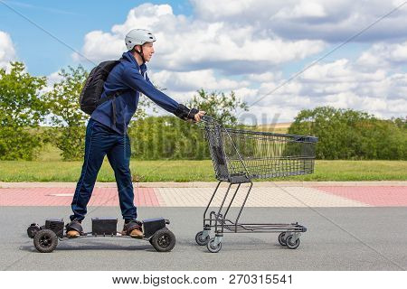 Dutch Teenage Boy  Rides On Electric Skateboard Pushing Shopping Cart Outdoors