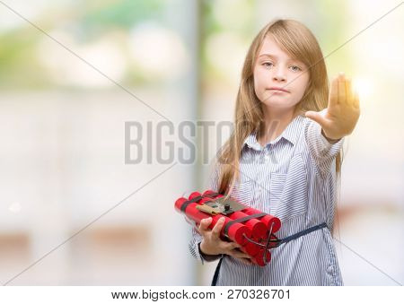 Young blonde child holding dynamite bomb with open hand doing stop sign with serious and confident expression, defense gesture