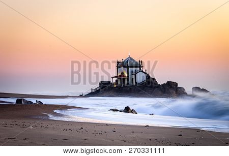 Side View Of Senhor Da Pedra Chapel At Sunset With Waves Crashing In The Sand. Golden Hour. Copy Spa