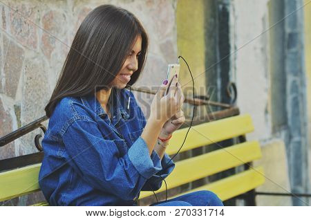 Young Beautiful Asian Girl Sitting On A Bench Talking On The Phone, Horizontal Photo, Campus