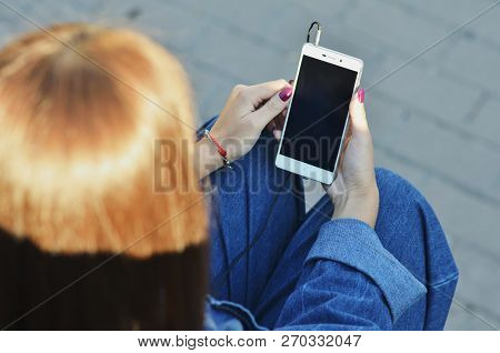 Smartphone Close-up In The Hands Of A Girl Dressed In Denim Clothing That Listens To Music In Headph