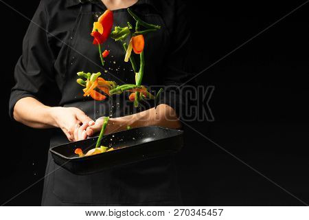 The Chef Prepares The Vegetables On The Pan. Black Background For Copying Text. Restaurant Business