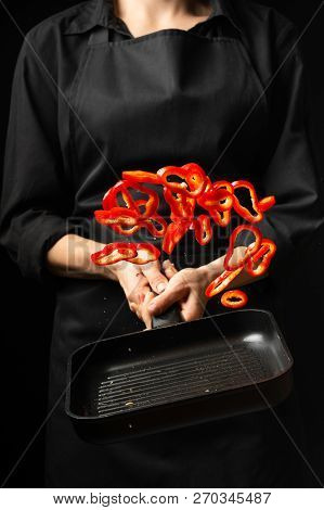 Professional Cook. Chef Preparing Dish With Red Sweet Pepper In A Pan, Paprika. On Black Background.