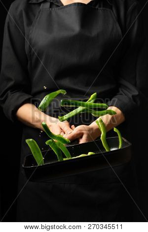 Professional Cook. He Prepares A Dish With Green Sweet Peppers In A Saucepan. On Black Background, M