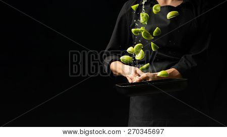 The Chef Cooks Green Tomatoes On The Pan. Black Background For Copying Text. Restaurant Business And
