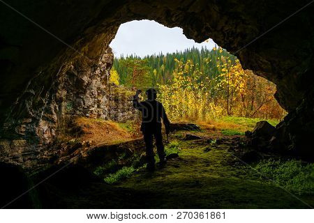 Silhouette Of A Geologist Examining A Mineral Sample Found In A Cave, On The Background Of An Entran