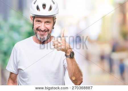 Middle age senior hoary cyclist man wearing bike safety helment isolated background doing happy thumbs up gesture with hand. Approving expression looking at the camera with showing success.