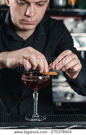 Bartender Making Boulevardier Cocktail Finishing Cocktail Putting Orange Slice On Top. Bar On A Back