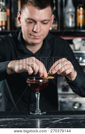 Bartender Making Boulevardier Cocktail Finishing Cocktail Putting Orange Slice On Top. Bar On A Back
