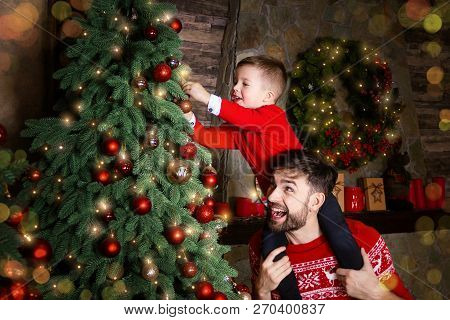 Happy Father And Son Enjoying Decorating Christmas Tree With Christmas Balls And Light Garland Prepa