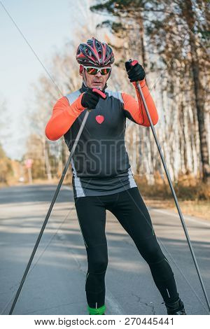 Training An Athlete On The Roller Skaters. Biathlon Ride On The Roller Skis With Ski Poles, In The H