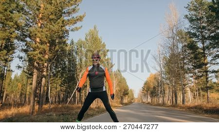 Training An Athlete On The Roller Skaters. Biathlon Ride On The Roller Skis With Ski Poles, In The H