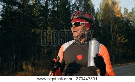 Training An Athlete On The Roller Skaters. Biathlon Ride On The Roller Skis With Ski Poles, In The H