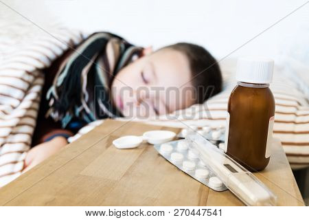 Young Boy Wearing Sweater And A Scarf Sleeping In His Bed While Having A Flu. Meds And Syrips On A W