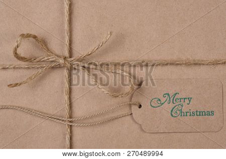 Flat lay plain brown paper wrapped Christmas Present with twine and tag with the words Merry Christmas.