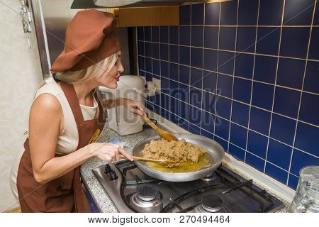 Young Beautiful Woman In An Apron Making Cake With Cream And Berries At The Kitchen