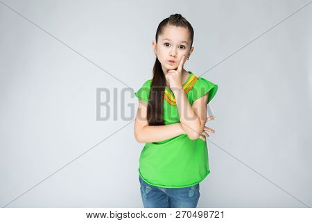 Girl On A Gray Background Put Her Finger To Her Cheek.