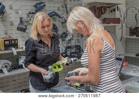 Beautiful Female Is Shopping For Diy Tools At Hardware Store. Smiling Saleswoman Shows Her A Drill. 