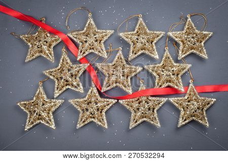 Golden Stars Christmas Decorations On A Gray Background With A Red Ribbon Exactly Lying