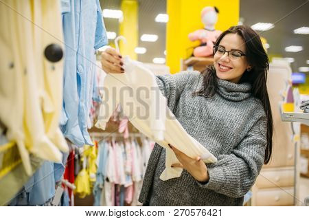 Happy future mother choosing clothes in the store