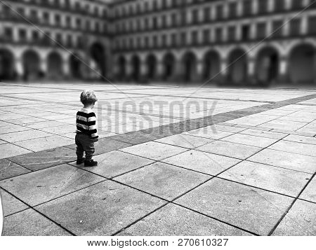 A Young Child Standing On His Back Alone In The Middle Of A Square And Beside A Line Of Cobblestone 