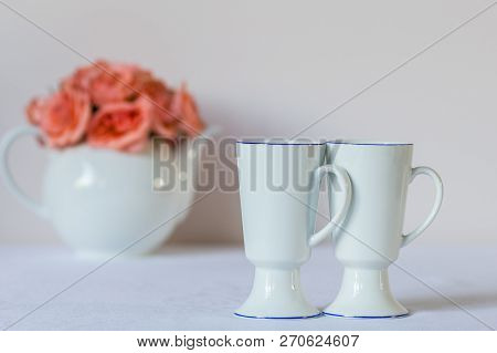Two White Cups Close-up Together And Teapot With Roses On A Background.