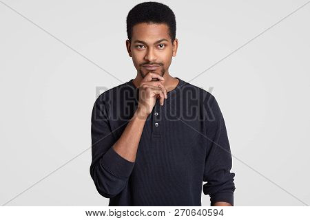 Shot Of Serious Male Entrepreneur Holds Chin, Has Afro Hairstyle And Dark Skin, Looks Seriously At C