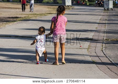 Young Girl Walking On A Footpath Of A Pedastrian Zone, Hand By Hand With Her Baby Brother. Narlidere