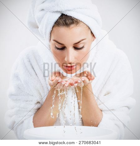Young Woman Washing Face With Clean Water. Over Gray Background.