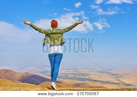 Travel Concept. Woman In A Mountains Standing In The Distance With Her Back To The Camera And Her Ar