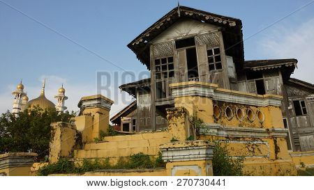 Old abandoned traditional malay house with a mosque in the background