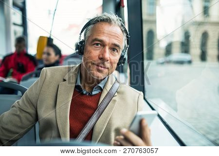 Mature Tired Businessman With Heaphones And Smartpone Travelling By Bus In City.