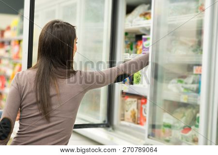 Woman taking deep frozen food from a freezer in a supermarket